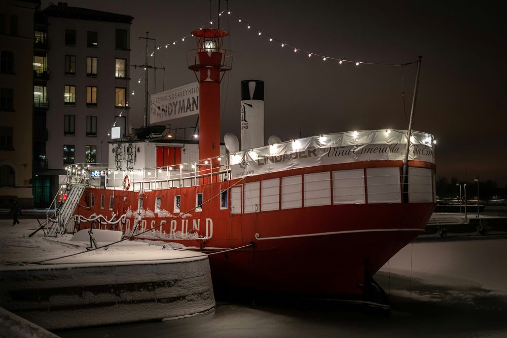 Rotes Feuerschiff im vereisten Hafenbecken von Helsinki bei Nacht, mit Lichterketten geschmückt