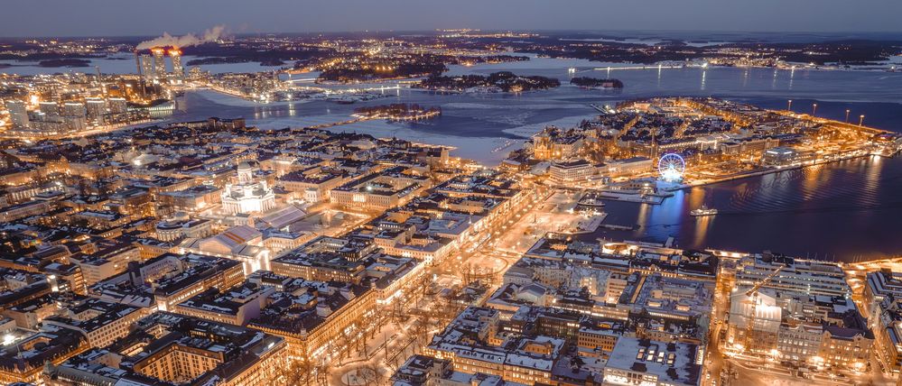 Luftbild der Innenstadt von Helsinki an einem Winterabend, beleuchtete Straßenzüge und vereistes Hafenwasser
